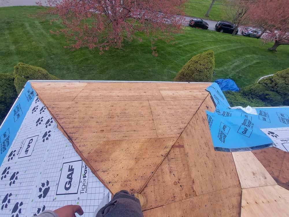 A person is laying plywood on top of a roof.