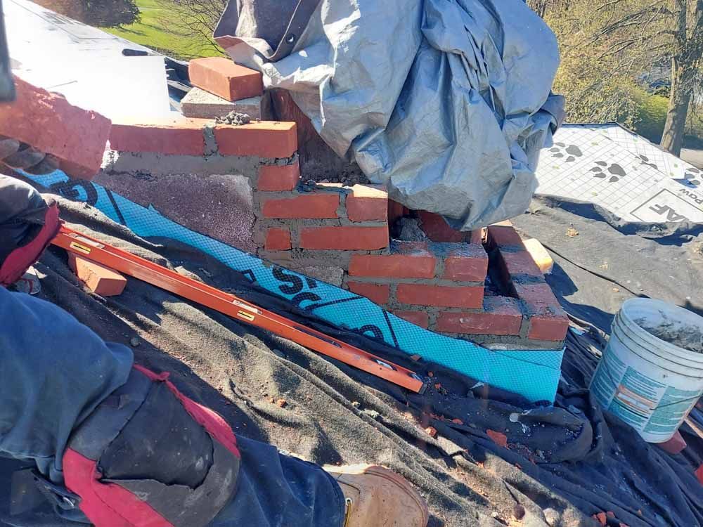 A person is laying bricks on top of a roof.