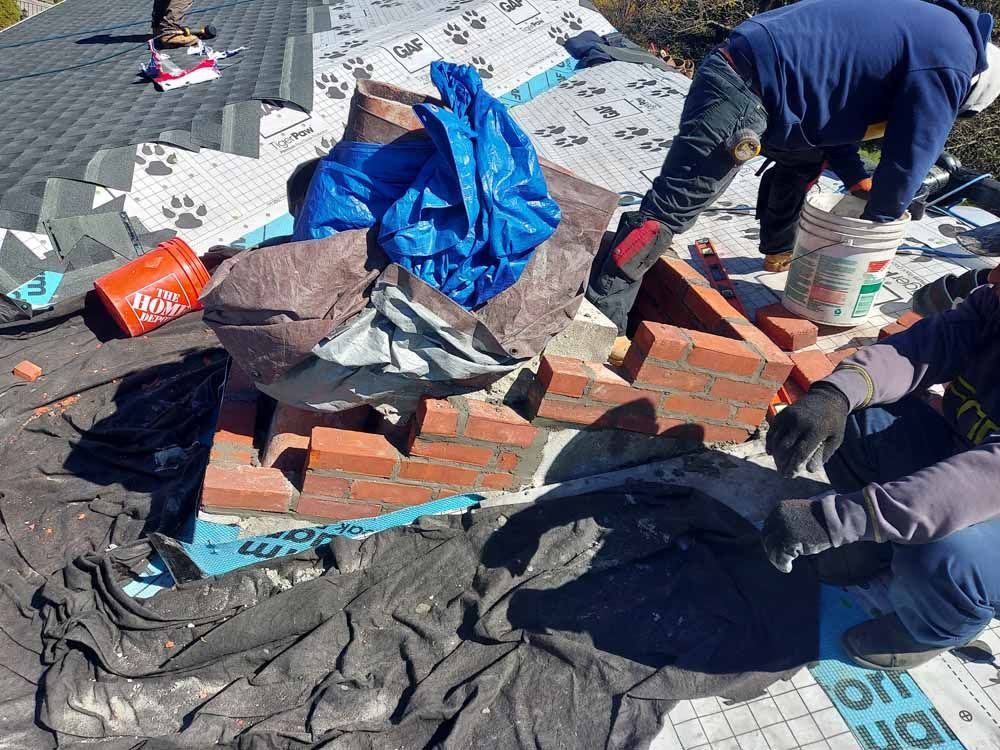 Two men are working on a brick chimney on a roof