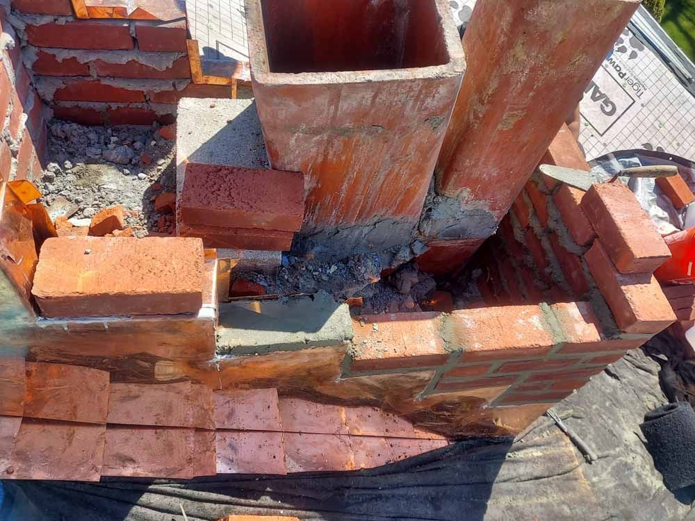 A brick chimney is being built on top of a roof.