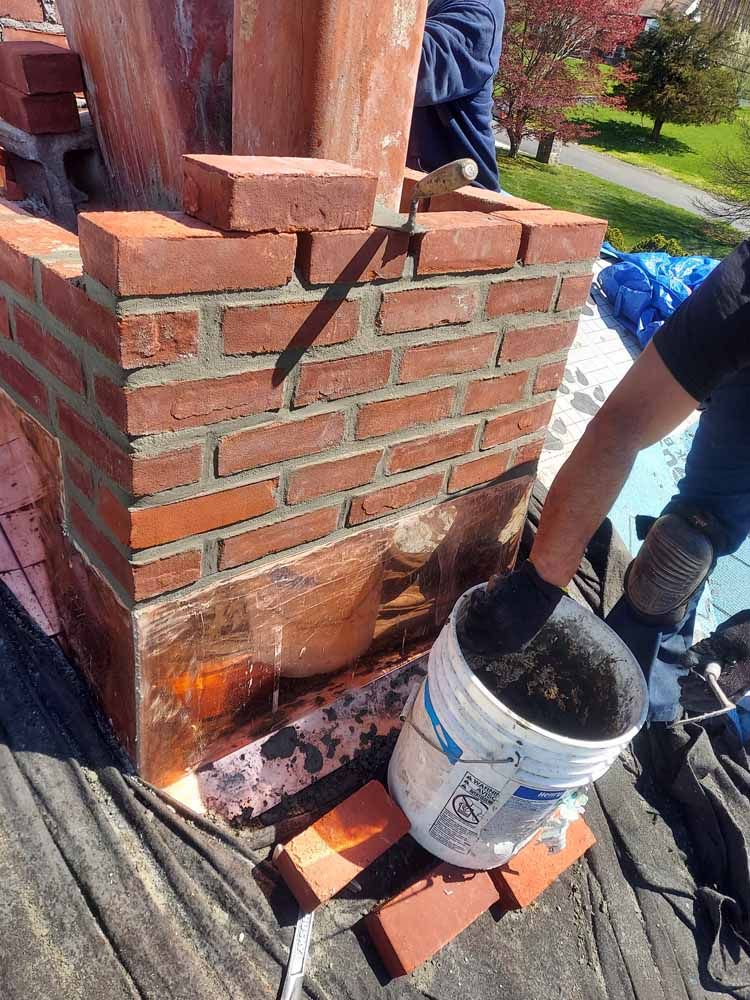 A man is laying bricks on top of a brick chimney.