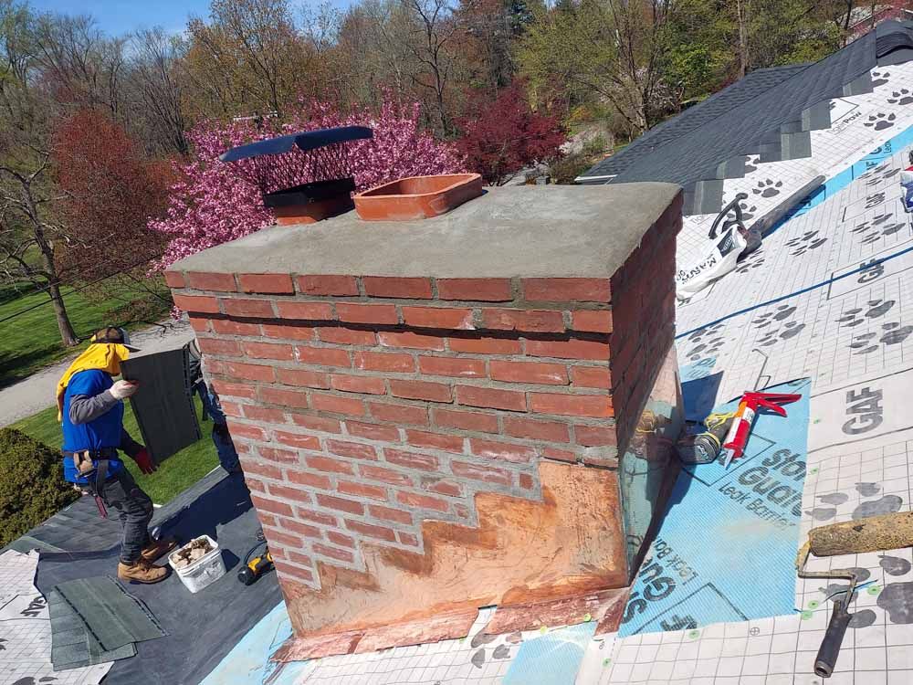 A man is working on a brick chimney on a roof.