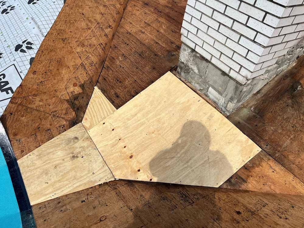 A piece of wood is sitting on top of a brick wall next to a chimney.