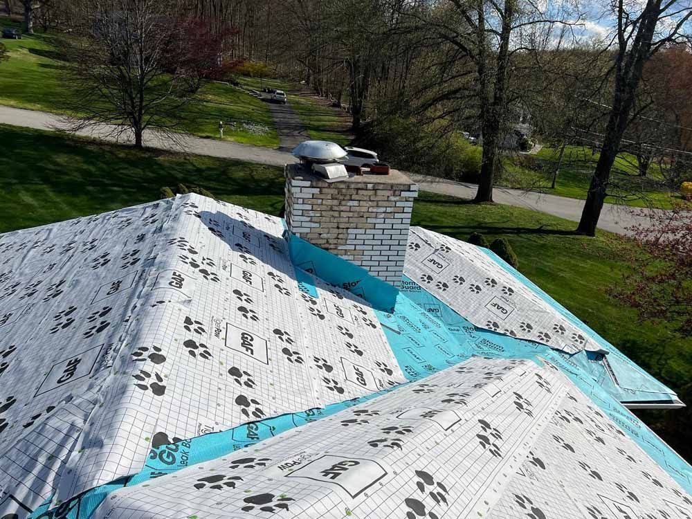 The roof of a house is being covered with a blue tarp.