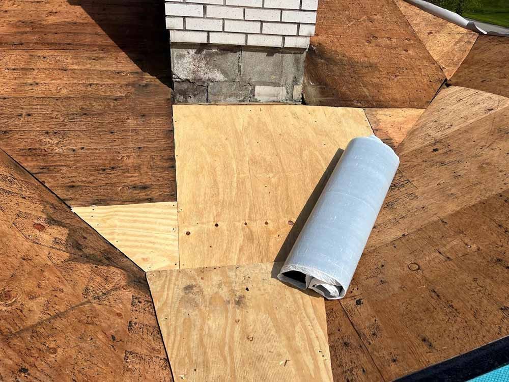 A roll of plywood is sitting on top of a wooden roof next to a chimney.