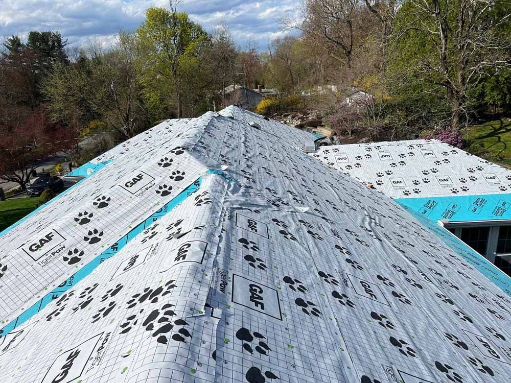 The roof of a house is being covered with a roofing material.