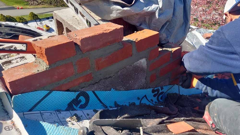 A man is laying bricks on top of a brick wall.