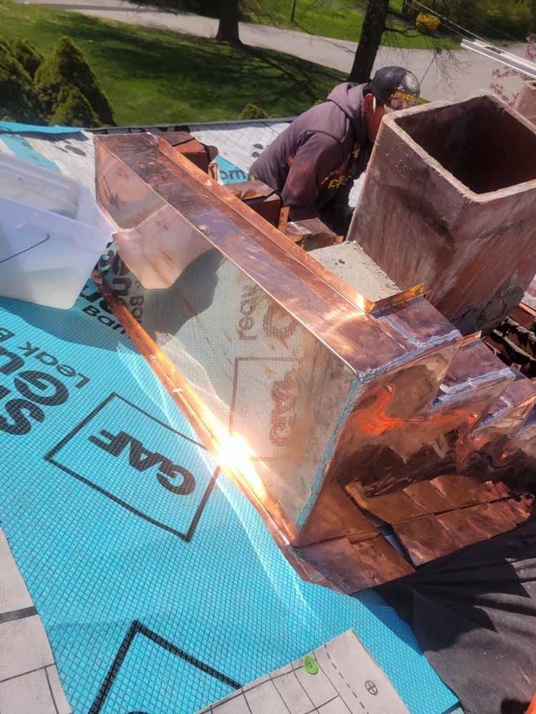 A man is working on a copper chimney on a roof.