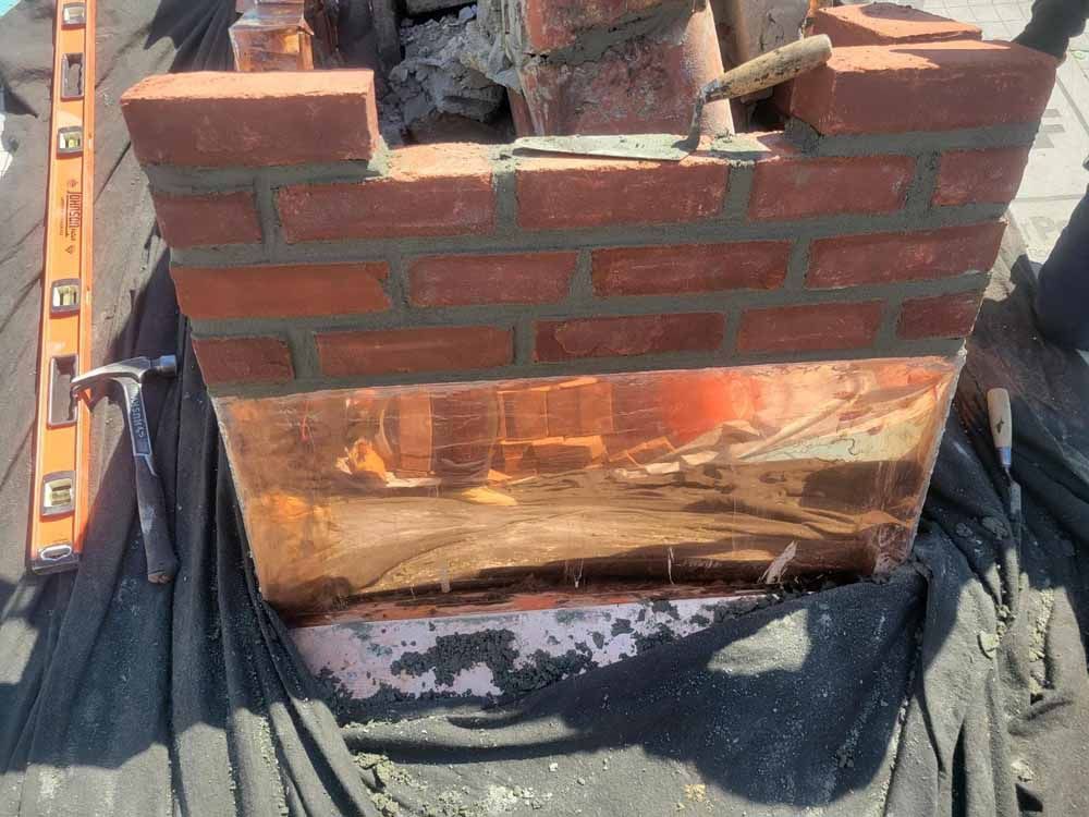 A brick chimney with a copper roof is being built on a roof.