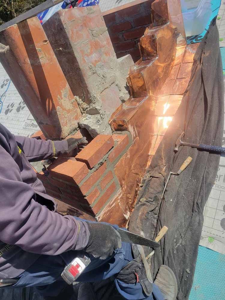 A man is working on a brick wall with a hammer and saw.