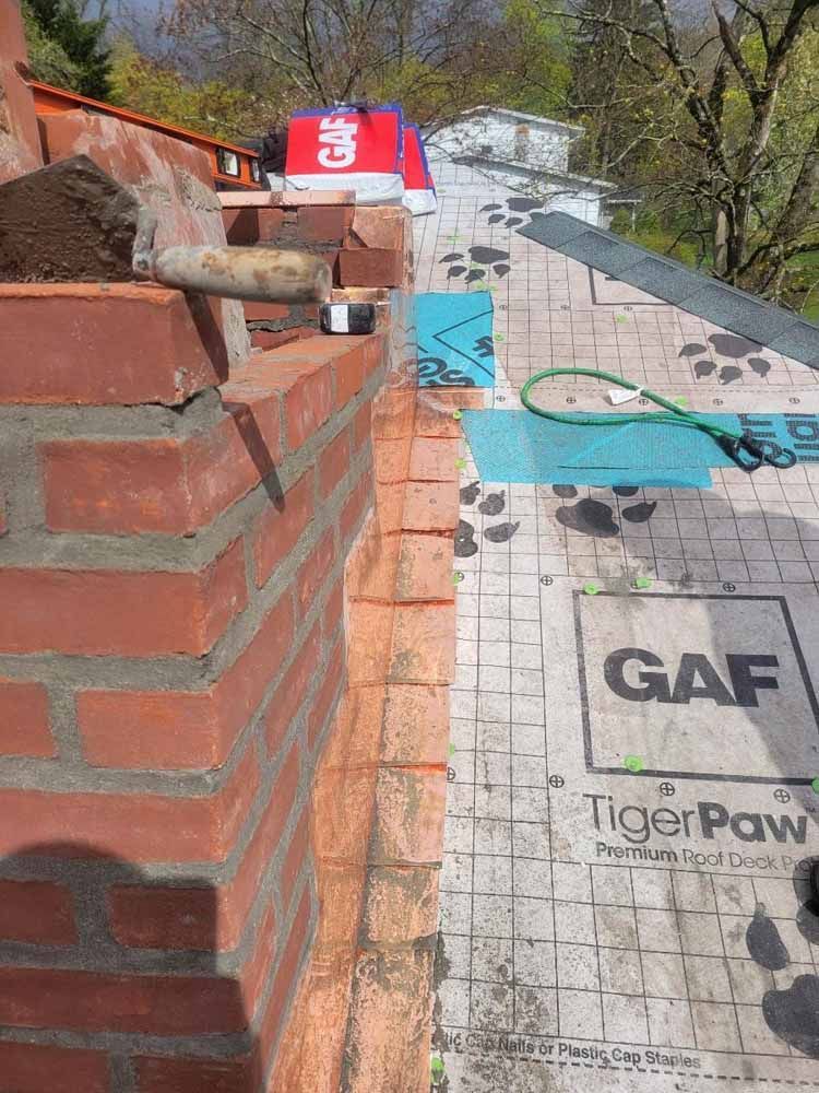 A brick wall is being built next to a tigerpaw roofing material.