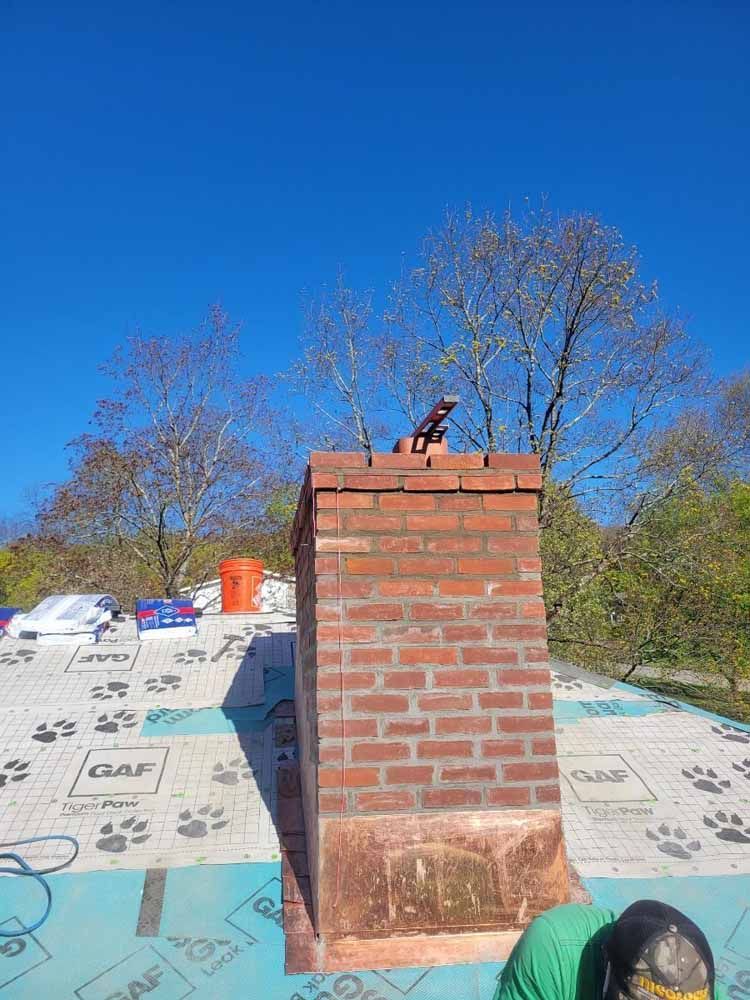 A man is working on a brick chimney on a roof.