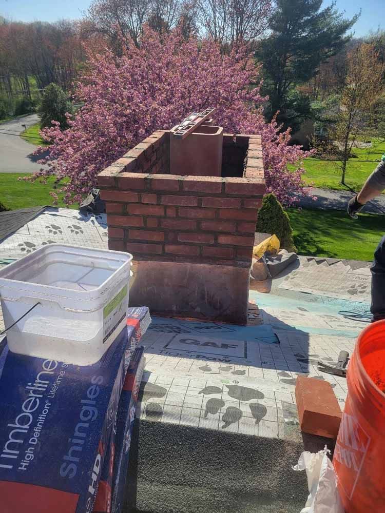 A brick chimney is being built on top of a roof.