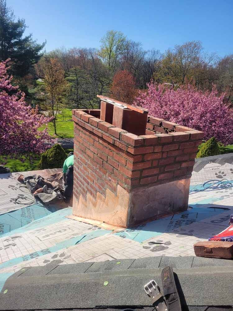 A brick chimney is being built on top of a roof.