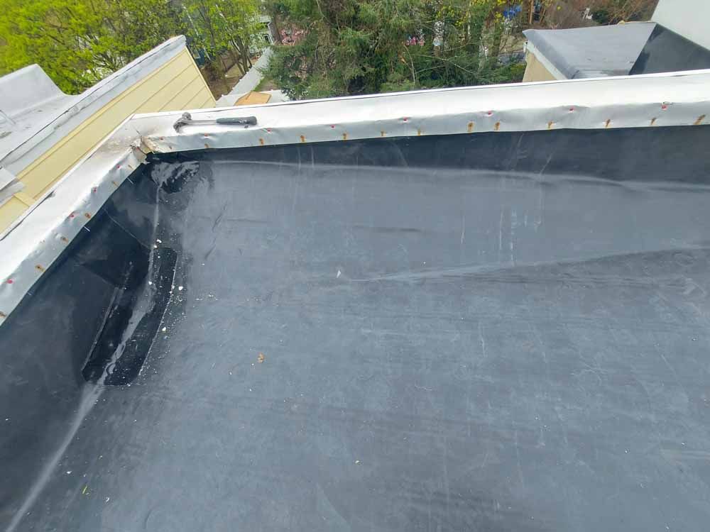 A close up of a black roof with trees in the background.