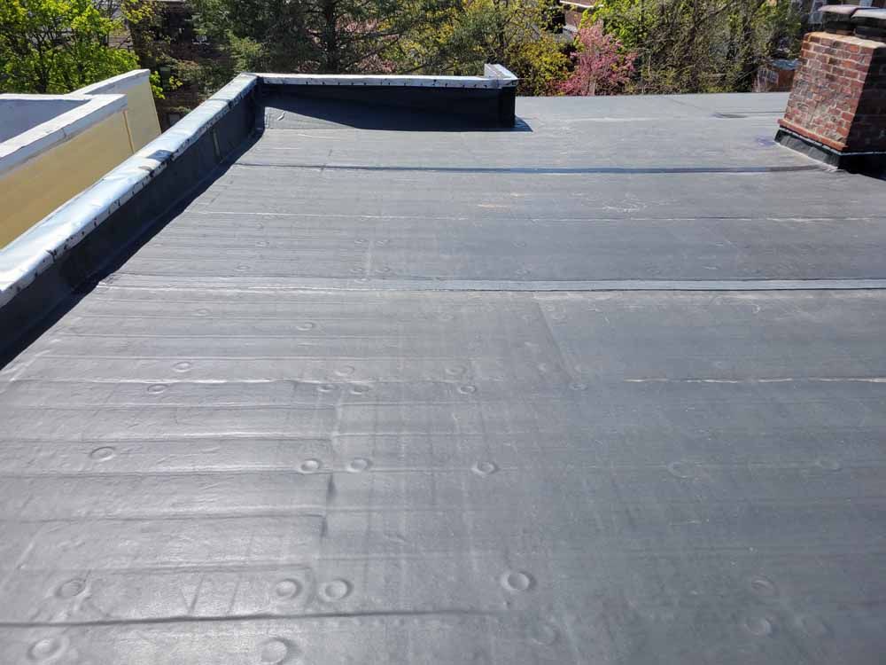 A black roof with a chimney and trees in the background