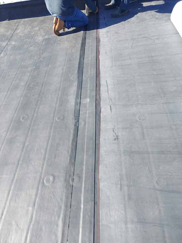 A person is kneeling on a roof with a black line on it.