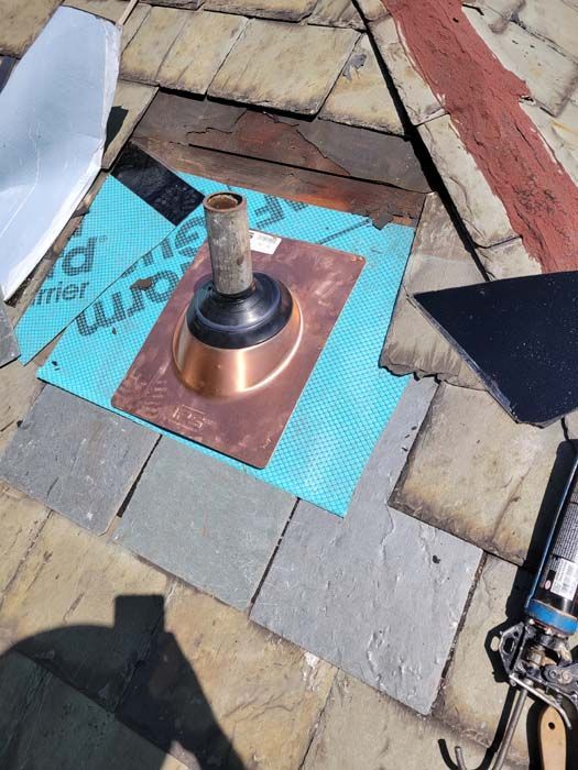 A copper pipe with a plunger on top of it is sitting on a brick floor.