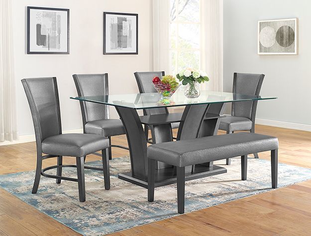 Modern dining set with glass-top table, gray chairs, and bench on a blue rug in a bright room
