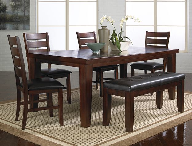 Dark wood dining table with four chairs and a bench on a light rug in a bright room