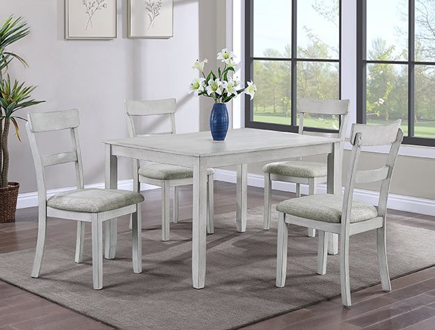 White dining set with four chairs and a vase of flowers in a bright room by large windows