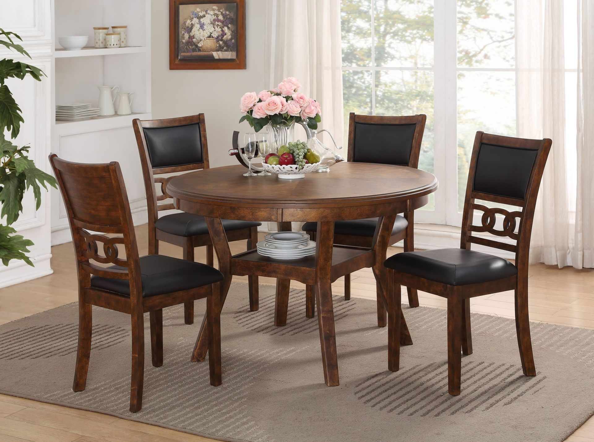 Round wooden dining table with four black chairs in a bright living room, pink flowers centerpiece