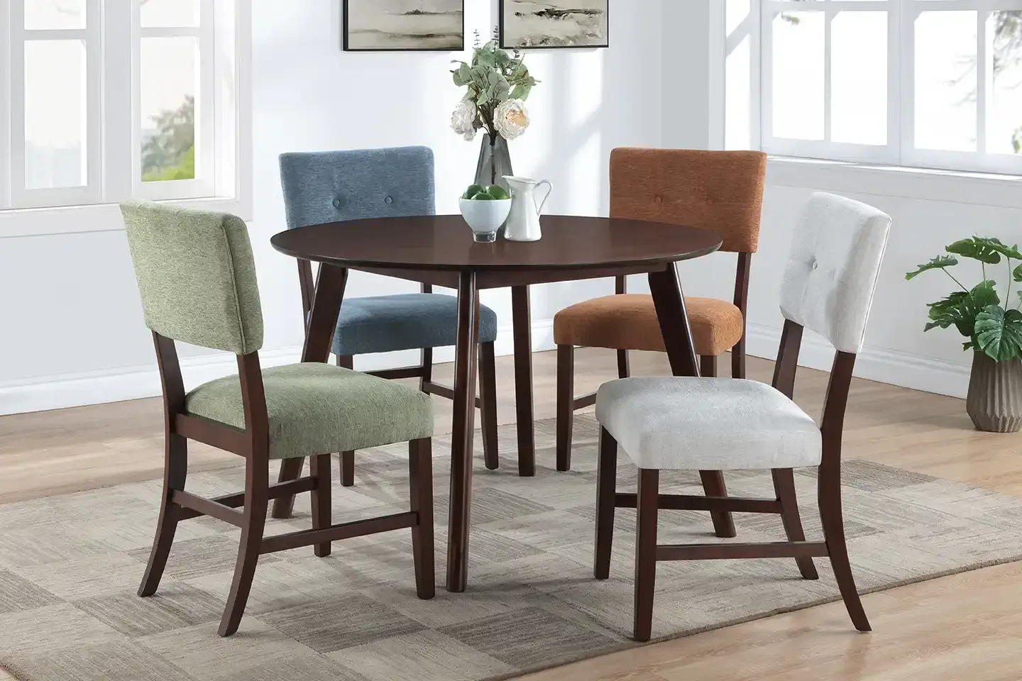Round dining table with four upholstered chairs in a bright room with windows and a rug