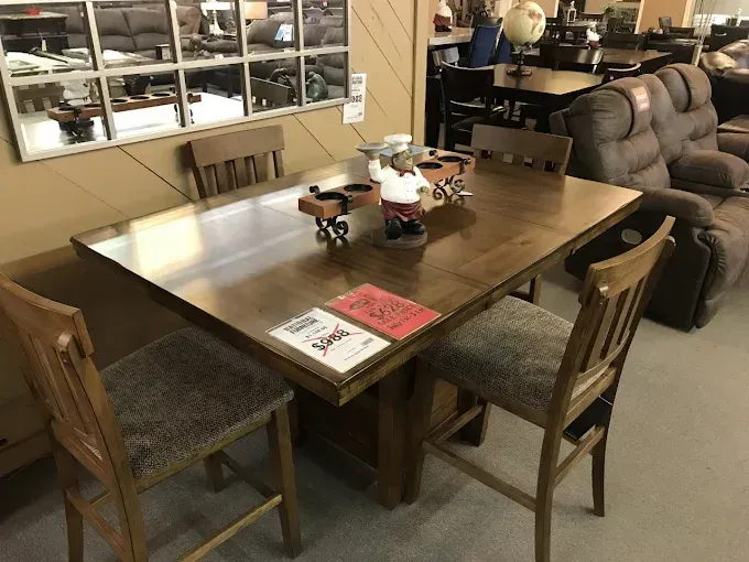 Dining room with wooden table, chairs, and a couch in the background.