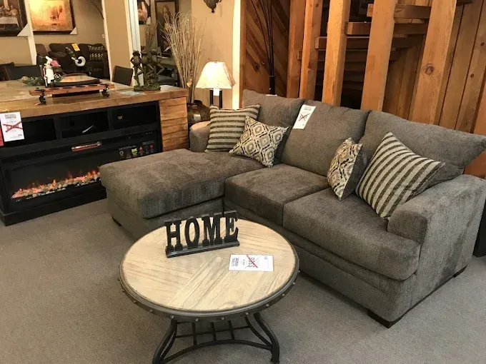 Gray sectional sofa and round coffee table in a cozy rustic living room with a fireplace.