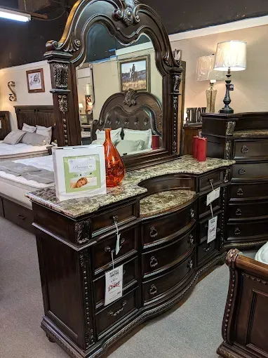 Dark wood dresser with ornate mirror in a furniture store, with lamps and decor on top.