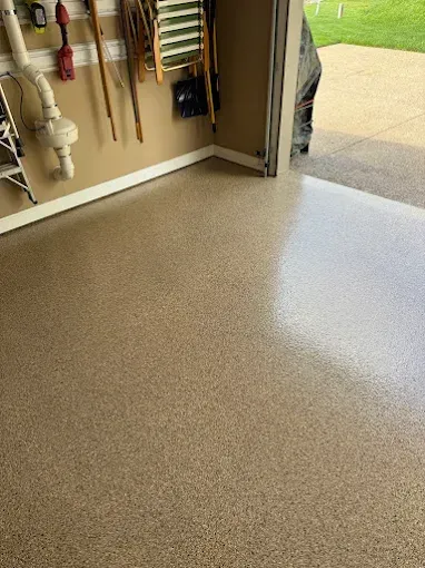 Garage with beige epoxy floor. Tools on wall, open door to outside, light reflecting on the floor.