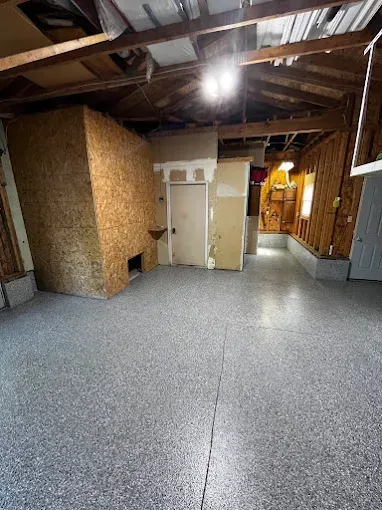 Spacious garage with epoxy floor, water heater, refrigerator, storage, and a door. Gray walls.