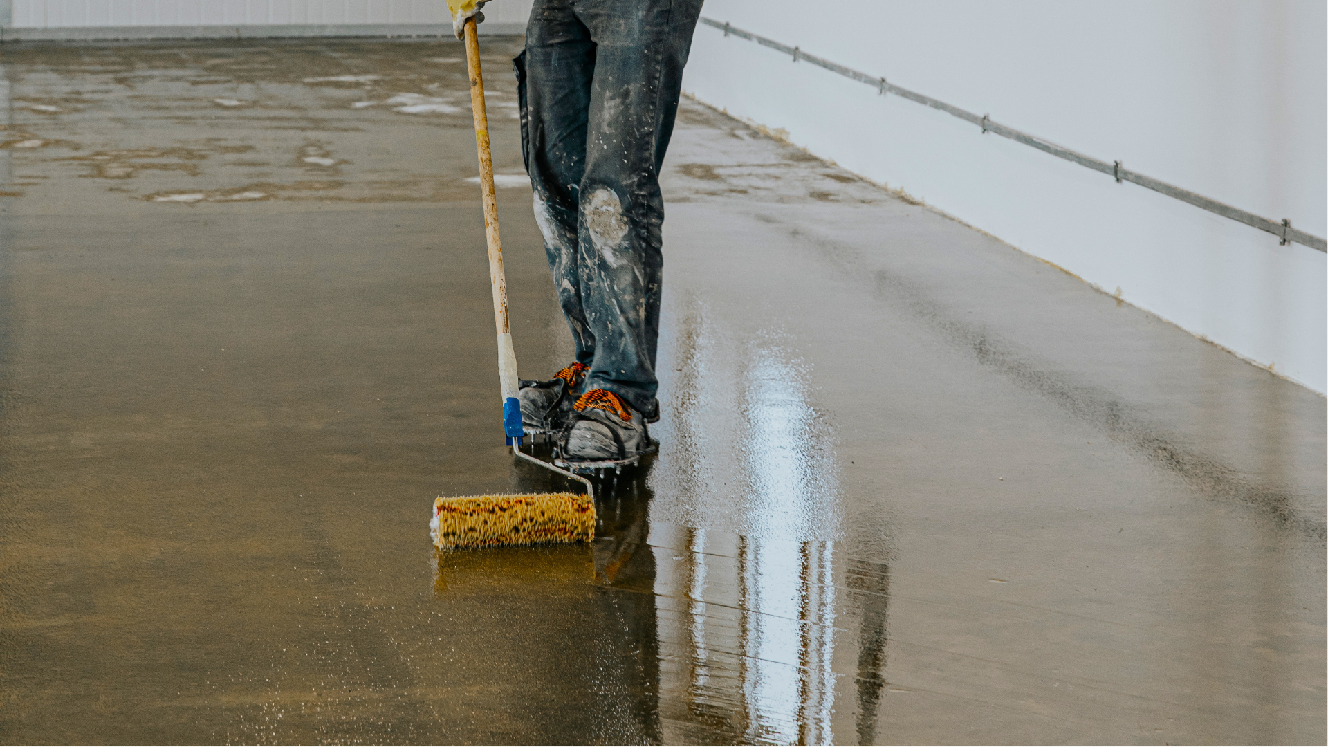 Person with paint roller applying sealant to a concrete floor.