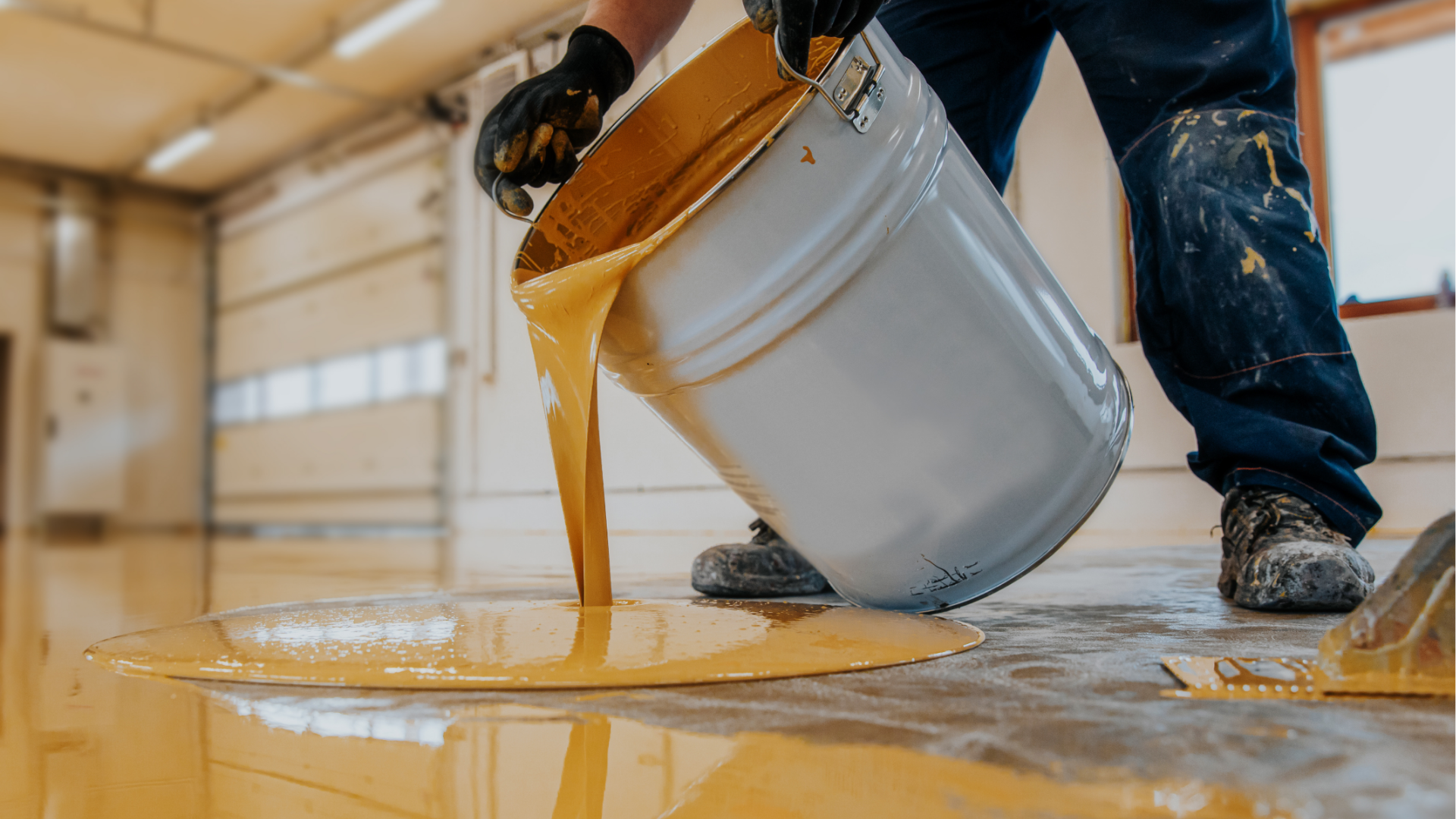 Person pouring yellow epoxy from a bucket onto a concrete floor.