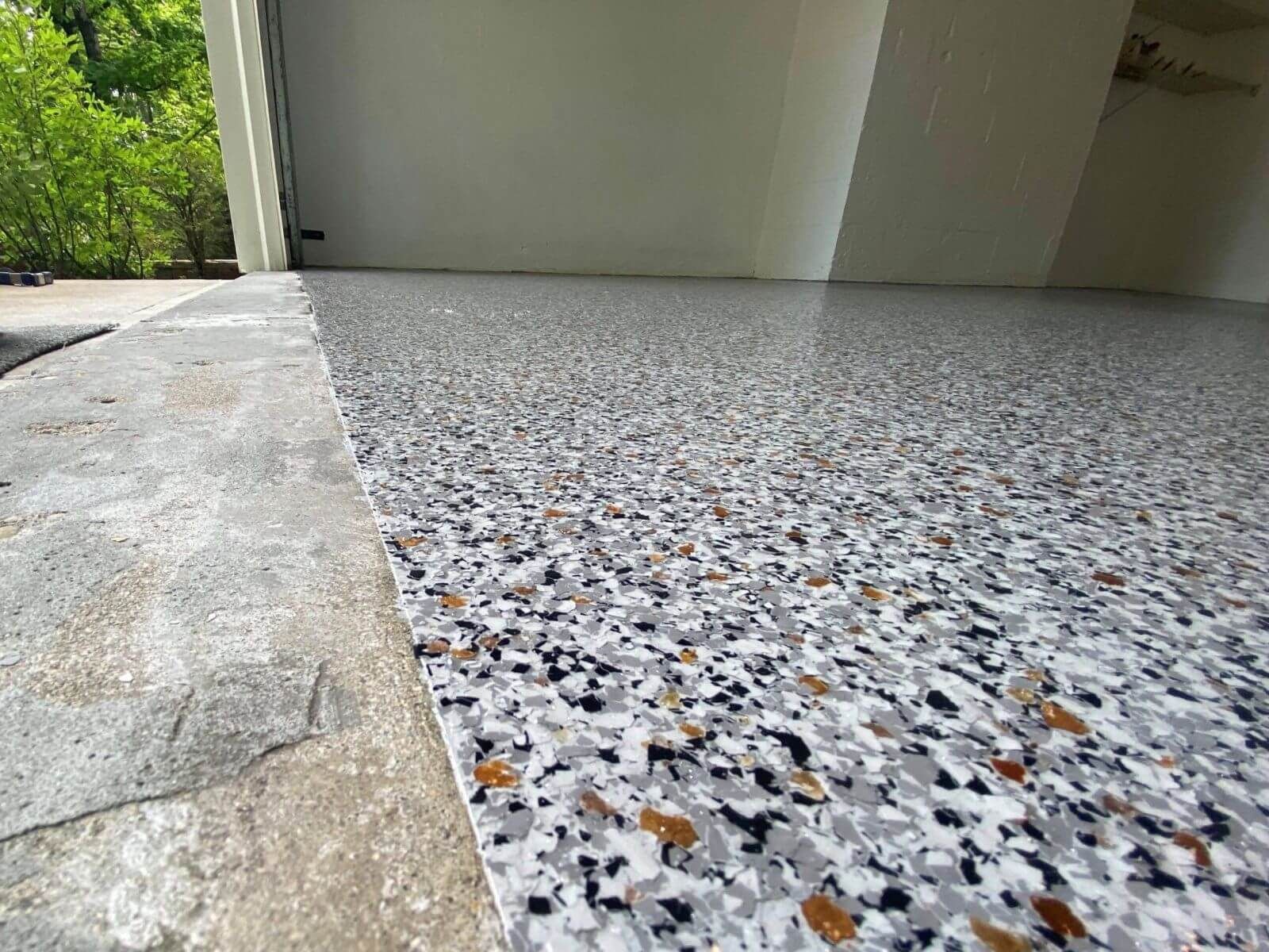 Epoxy floor with gray, black, and brown chips inside a garage, next to a concrete exterior.