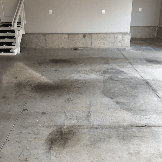 Concrete garage floor with stains and stairs to the left; light beige walls.
