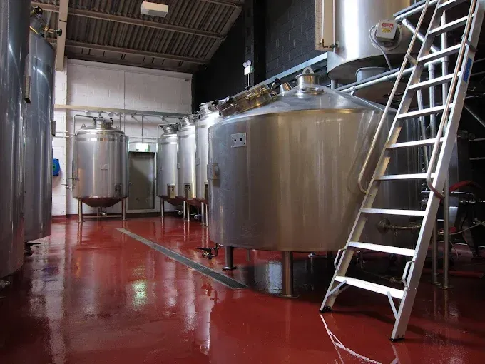 Stainless steel tanks in a brewery with a red floor and a ladder.