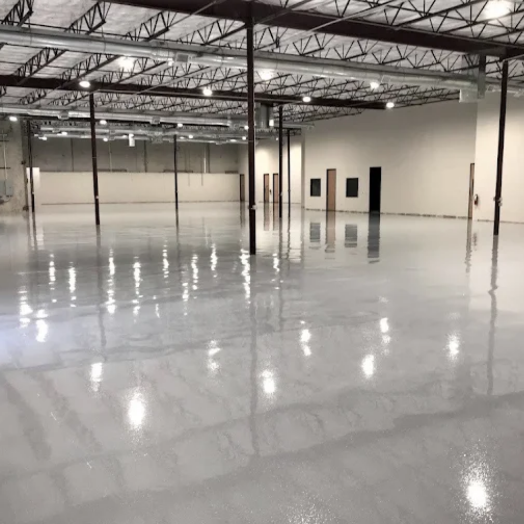 Empty, brightly lit warehouse interior with a shiny, gray floor and structural supports.