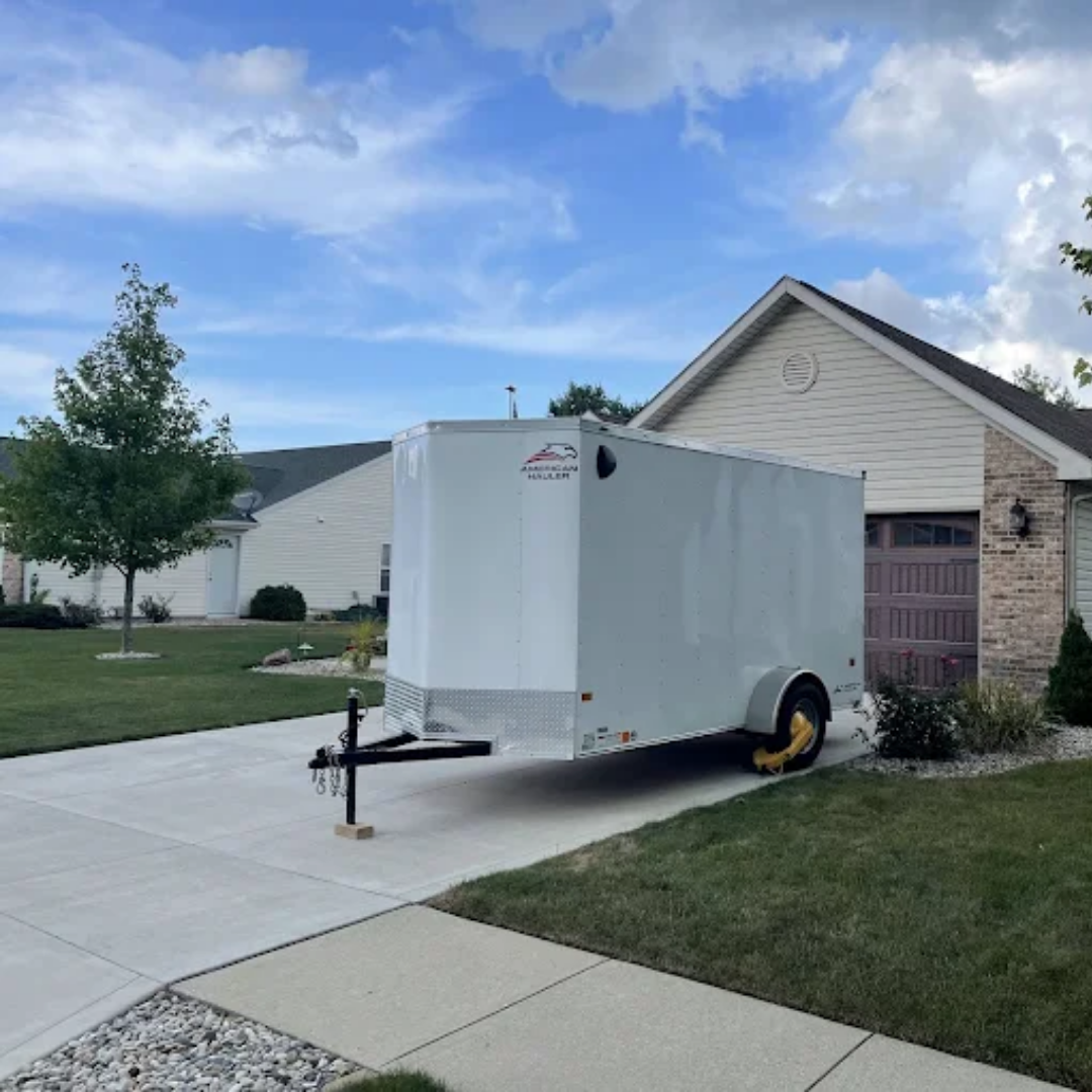 White cargo trailer parked on a driveway in front of a house on a sunny day.