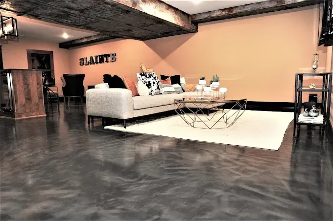 Modern living room with grey metallic epoxy floor, cream couch, orange wall, geometric coffee table.