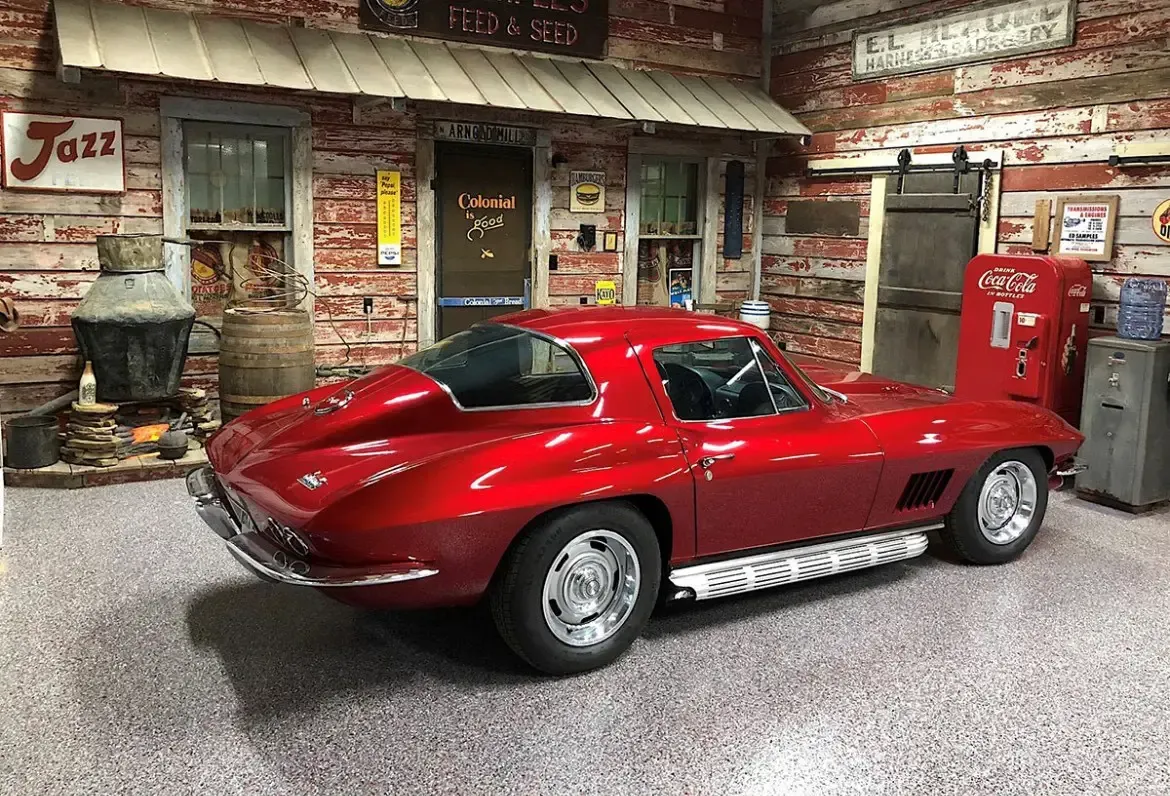 Red vintage Corvette in a garage setting with a rustic facade.