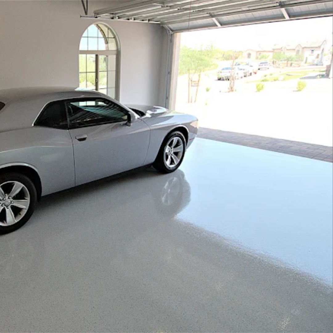 Silver muscle car parked in a clean, light-colored garage with the door open to the outside.