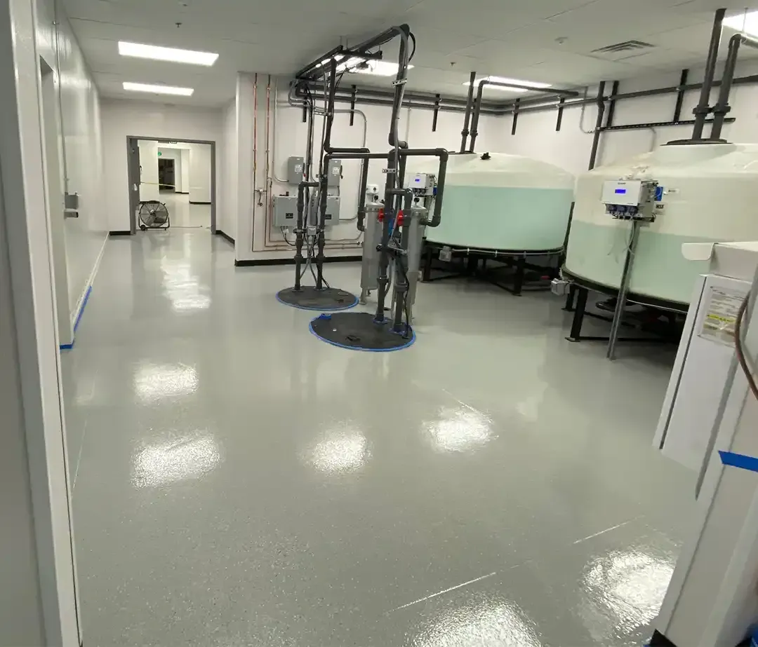 Large, empty industrial space with shiny gray floor, black stripe, and overhead lighting.