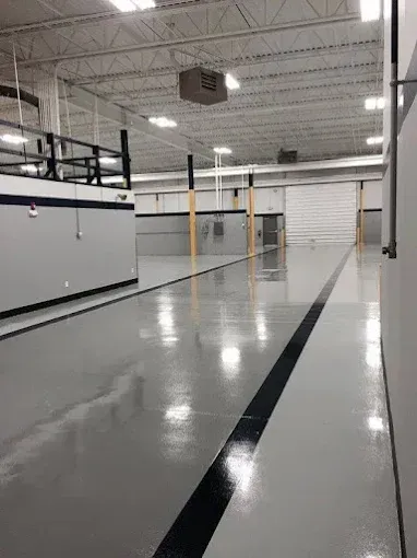 Large, empty industrial space with shiny gray floor, black stripe, and overhead lighting.