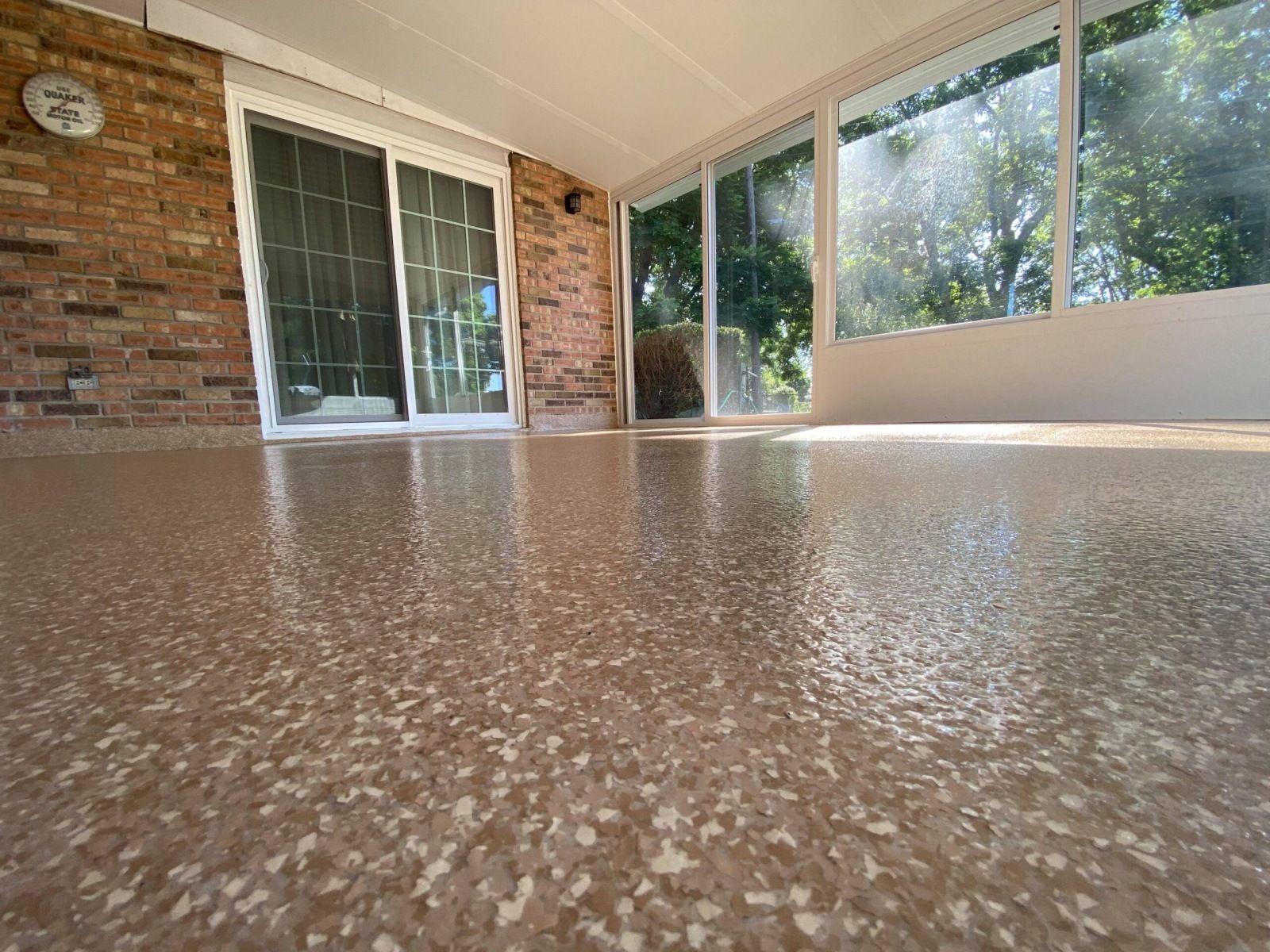 Sunroom with shiny speckled floor, brick wall, sliding glass door, and windows overlooking trees.
