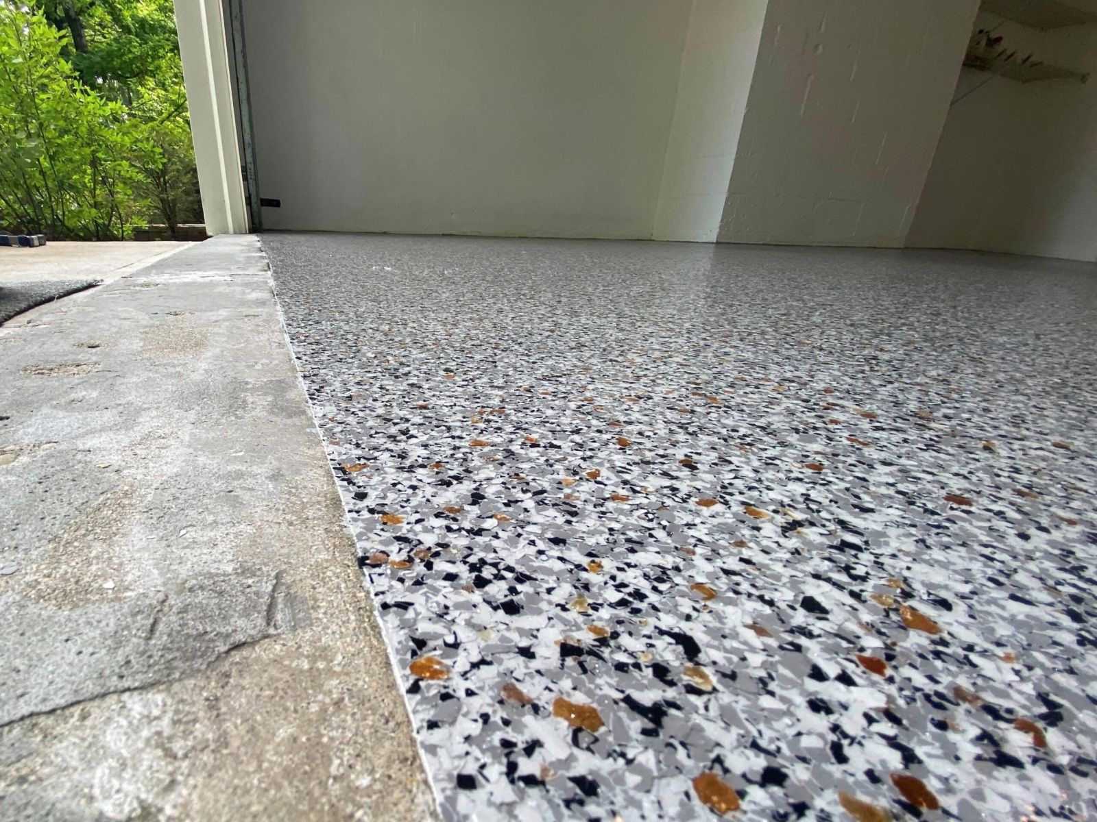 Close-up of a garage floor with a speckled, epoxy coating in shades of gray, white, black, and brown.