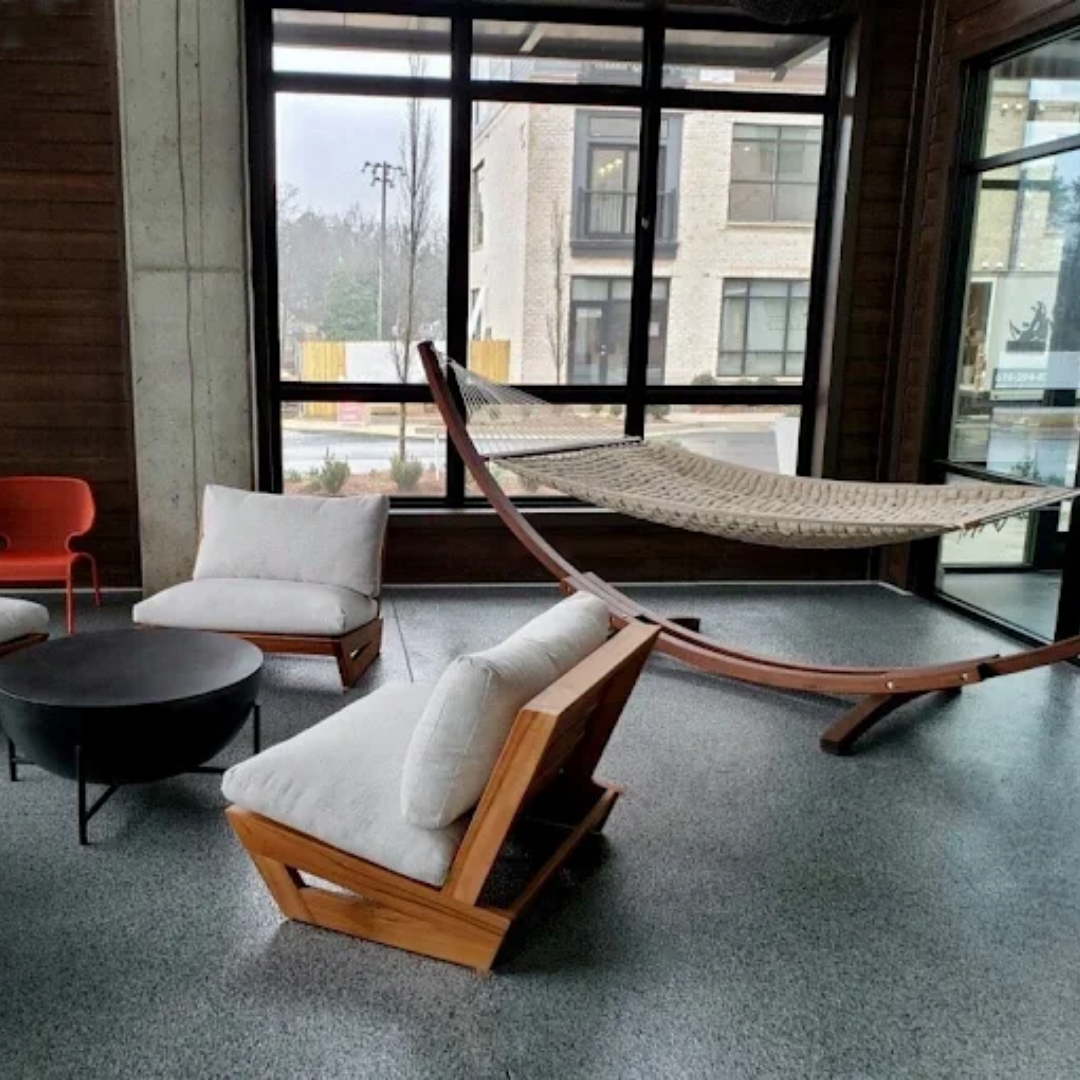 A lounge area with wooden chairs, a hammock, and a black coffee table in front of a window.