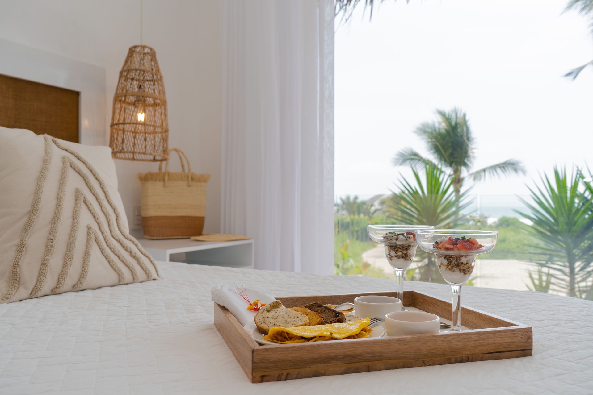Breakfast tray on a bed in a bright room with a view of palm trees.