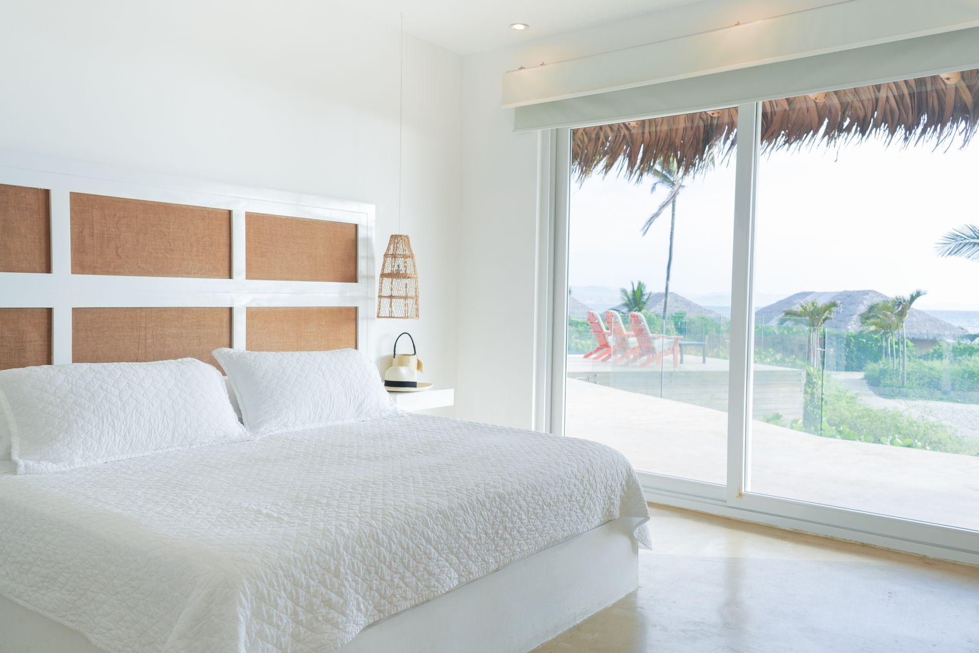 White bedroom with bed, large windows, and a beach view.