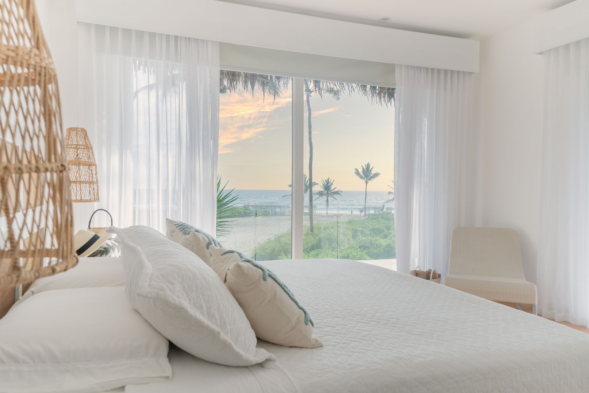 Bedroom with a white bed, sheer curtains, and a beach view.